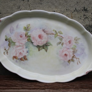 May include: An oval porcelain tray with a scalloped edge and pink rose floral design. The tray has a pink rim and two handles.