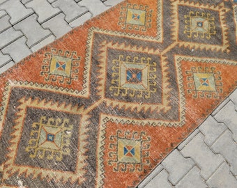 May include: A vintage rug with a geometric pattern in shades of orange, brown, and blue. The rug has a distressed look and is made of wool.