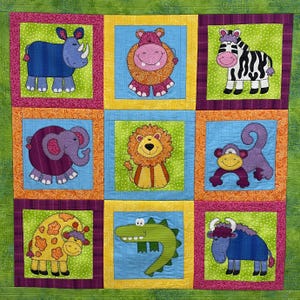 Op de afbeelding: Een patchwork quilt met negen vierkante panelen, elk met een ander stoffen applicatiedier, waaronder een blauwe neushoorn, roze nijlpaard, zebra, paarse olifant, leeuw, aap, giraf, groene krokodil en een blauwe buffel.