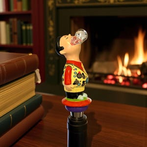May include: A novelty bottle stopper featuring a figurine of a man with a bubble-shaped glass orb emerging from his mouth. The figurine wears a yellow sweater with black and blue circles, a red shirt, and black pants. The stopper has a red, purple, and green base.