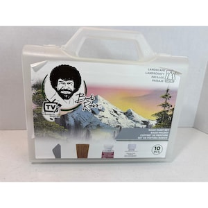 Könnte beinhalten: Ein durchsichtiger Kunststoffkoffer für ein 10-teiliges Bob Ross Basis-Malset. Das Etikett zeigt ein Porträt von Bob Ross, eine Berglandschaftsillustration sowie den Text "Bob Ross", "TV's Favorite Painter" und "Basic Paint Set".