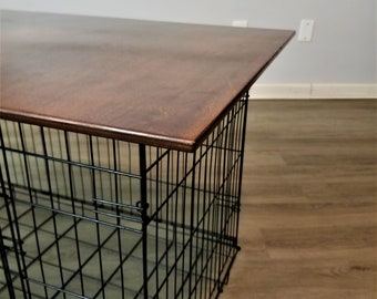 May include: A black wire dog crate with a dark brown wooden top. The crate is rectangular and has a grid-like design. The wooden top is smooth and appears to be stained. The crate is designed for pet containment.