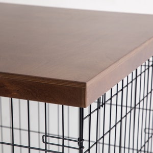 May include: A black metal dog crate with a brown wooden top. The crate has a wire mesh design and is suitable for a medium-sized dog.
