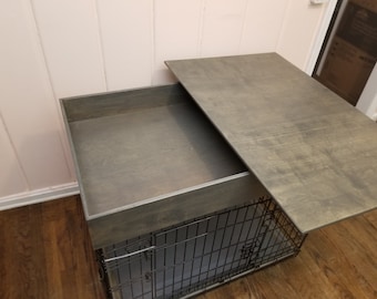 May include: A gray wooden crate with a hinged lid that opens to reveal a black metal dog crate. The crate is on a wooden floor.