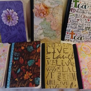 Puede incluir: Ocho cuadernos diferentes con varios diseños. Las cubiertas presentan patrones florales, mapas, texto religioso y palabras inspiradoras. Los cuadernos están encuadernados con cinta negra y dorada.