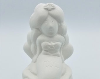 May include: A white ceramic mermaid figurine with long flowing hair, a seashell top, and a mermaid tail. The figurine is sitting on a cloud-like base and has a starfish in her hair.