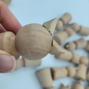 May include: A close-up of a wooden doll with a round head and two pointed ears. The doll is made of unfinished wood and is ready to be painted or decorated.