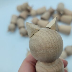 May include: A wooden toy cat with triangular ears. The cat is light brown and has a smooth, rounded body.