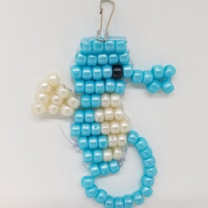 Peut inclure: Un porte-cl&eacute;s en forme d'hippocampe en perles bleues et blanches avec un fermoir argent&eacute;. L'hippocampe est fait de petites perles rondes et a un &oelig;il noir.