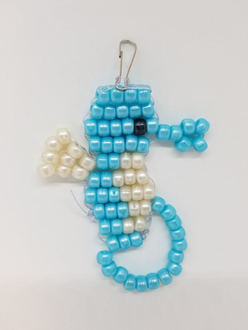 Peut inclure: Un porte-cl&eacute;s en forme d'hippocampe en perles bleues et blanches avec un fermoir argent&eacute;. L'hippocampe est fait de petites perles rondes et a un &oelig;il noir.