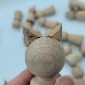 May include: A wooden toy with a round body and two triangular ears. The toy is made of light brown wood and has a smooth finish.