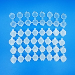 May include: A set of 48 clear plastic paint pots, arranged in rows on a blue background. The pots are small and round, with a lip around the top.
