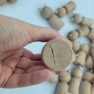 May include: A close-up of a wooden doll head with a crack down the center. The doll head is light brown and has a smooth surface.