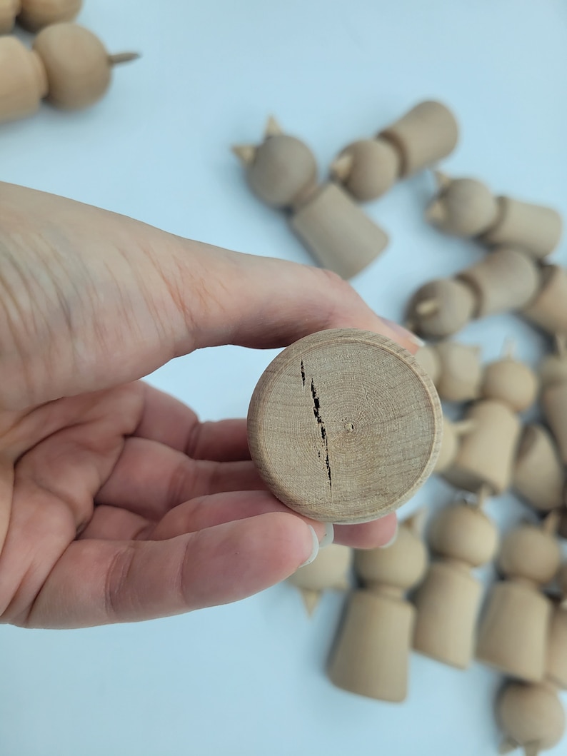 May include: A close-up of a wooden doll head with a crack down the center. The doll head is light brown and has a smooth surface.
