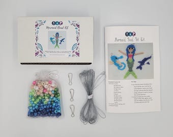 May include: A Mermaid Bead Kit containing a white box with a mermaid graphic, an instruction booklet, a clear bag of assorted colorful plastic beads, three metal lanyard hooks, and a coil of clear plastic lacing cord for crafting projects.