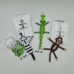 May include: Three assembled pony bead animal figures including a green lizard, a black and white zebra, and a brown monkey, accompanied by two plastic supply bags containing loose green and white beads, clear cord, and printed instruction sheets.