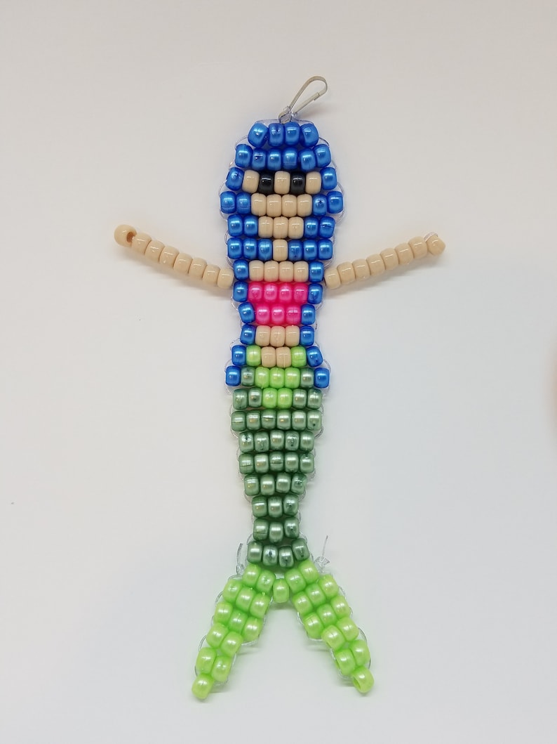 Peut inclure: Un charme de sir&egrave;ne en perles avec un haut bleu, un bikini rose et une queue verte. Le charme est fait de petites perles en plastique et a une boucle en haut pour l'accrocher.