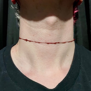 May include: A close-up of a person's neck with a thin red line of fake blood around it.
