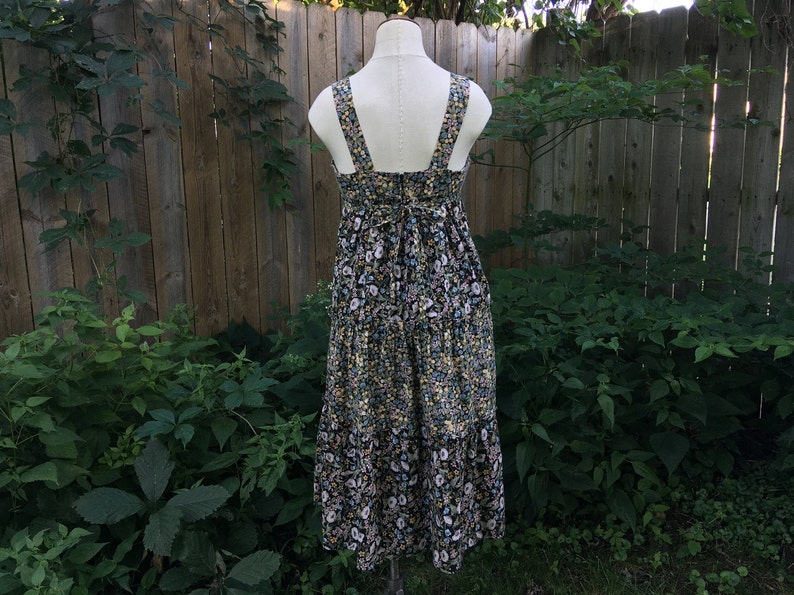 Puede incluir: Vestido midi con estampado floral sobre un maniqu&iacute;. El vestido presenta un fondo negro con un estampado de peque&ntilde;as flores blancas, azules y amarillas. Tiene un escote cuadrado, tirantes anchos y una falda escalonada. El vestido se exhibe al aire libre.