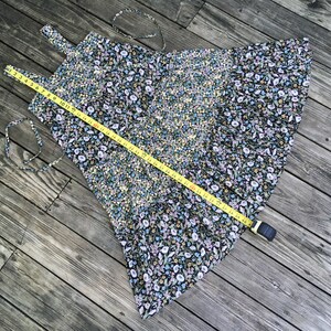Puede incluir: Un vestido negro con estampado floral con una cinta m&eacute;trica amarilla colocada encima. El vestido presenta un patr&oacute;n de peque&ntilde;as flores blancas, azules y amarillas. La cinta m&eacute;trica muestra una longitud de aproximadamente 122 cm.