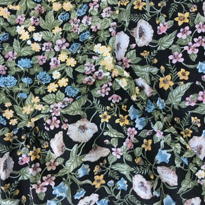 Puede incluir: Primer plano de una tela con un estampado floral. El dise&ntilde;o presenta un fondo negro con una variedad de flores en tonos blancos, rosas, amarillos y azules, junto con hojas verdes. La tela parece ser un material ligero.