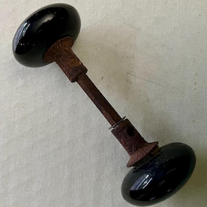 May include: Antique black glass door knob with a rusty metal stem. The oval-shaped knobs have a glossy finish. The stem and base show signs of age and wear, adding to the vintage aesthetic. A classic hardware piece.