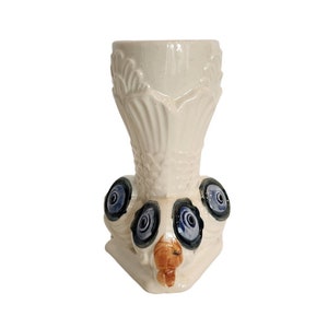 May include: White ceramic vase with blue and brown floral designs. The vase has a wide mouth and a narrow base.