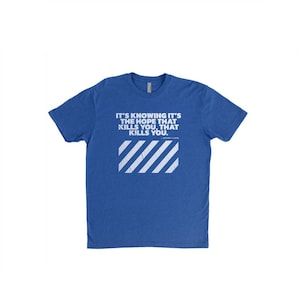 May include: Royal blue crew neck t-shirt. The front features white text: "IT'S KNOWING IT'S THE HOPE THAT KILLS YOU, THAT KILLS YOU." Below the text is a white, diagonal striped rectangle.