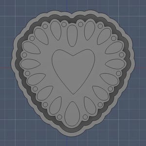 Op de afbeelding: Een grijs hartvormig ontwerp met een hart in het midden, omgeven door een decoratieve rand. De rand heeft druppelvormen en kleine cirkels. Het ontwerp staat tegen een blauwe rasterachtergrond.