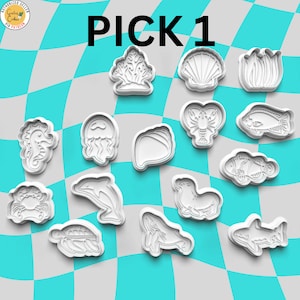 Könnte beinhalten: Ein Set mit 13 weißen Plastik-Ausstechern in Form verschiedener Meeresbewohner, darunter ein Seepferdchen, eine Qualle, eine Muschel, ein Hummer, ein Fisch, ein Delfin, ein Wal, ein Hai, eine Krabbe, eine Schildkröte und eine Koralle. Die Ausstecher sind auf einem karierten blau-weißen Hintergrund angeordnet. Der Text "PICK 1" ist oben im Bild in Schwarz geschrieben.