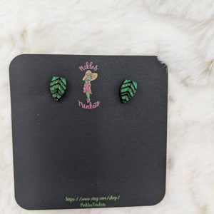 May include: A pair of green and black leaf-shaped earrings on a black card with the text "Pickles Tunkets" and a website address.