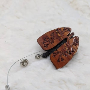 May include: A wooden brown and black lung-shaped badge reel with a clear plastic strap and silver metal clips.