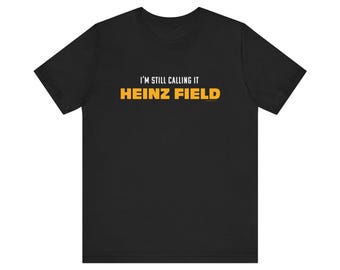 Puede incluir: Camiseta negra con el texto "I'M STILL CALLING IT" encima de "HEINZ FIELD" en amarillo. La camiseta es de manga corta y cuello redondo.