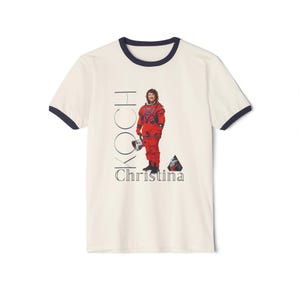 May include: Cream-colored ringer t-shirt with a navy blue collar and sleeve trim. The shirt features an image of an astronaut in a red spacesuit, with the name "KOCH" and "Christina" printed in black.
