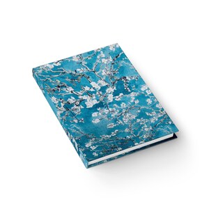 May include: A rectangular hardcover journal with a teal cover. The cover features a floral design in white and silver, resembling a painting of blossoming branches. The journal has a white edge and a textured background.