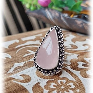Puede incluir: Un anillo de plata con una piedra rosa en forma de lágrima engastada en un engaste de cuentas.