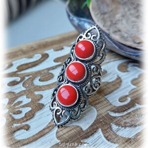 Puede incluir: Un anillo de plata con un diseño de filigrana y tres piedras rojas. El anillo está sobre una superficie de madera.