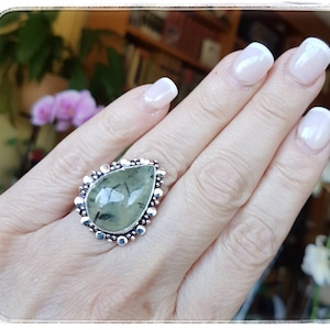 May include: A silver ring with a teardrop-shaped green stone set in a beaded bezel.