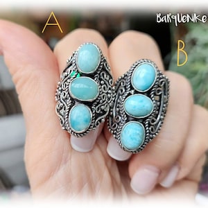 May include: Two silver rings with blue and green gemstone accents. The rings are on a person's fingers. The rings are labelled A and B.