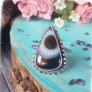 May include: A silver ring featuring a teardrop-shaped black and white agate stone. The stone has a distinctive eye-like pattern.