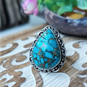 Puede incluir: Un anillo de plata con una gran piedra turquesa en forma de lágrima. La piedra tiene un patrón de mármol azul y dorado.