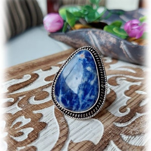 Puede incluir: Un anillo de plata con una piedra preciosa azul y blanca. La piedra preciosa tiene forma de lágrima y está engastada en plata.