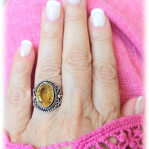 May include: A silver ring featuring an oval yellow gemstone set within an intricate filigree design.