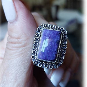 May include: A silver ring featuring a purple and blue gemstone set within an ornate silver frame.