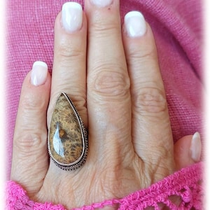 May include: A silver ring featuring a teardrop-shaped brown and white stone set in a silver bezel. The ring is worn on a finger.