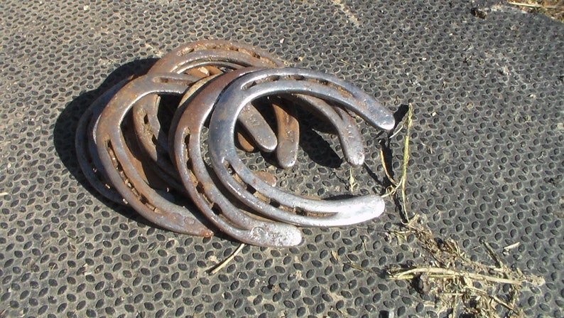 May include: A group of five rusty horseshoes stacked on top of each other on a black textured surface.