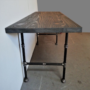 May include: A long, dark wood table with black metal pipe legs. The table is made of reclaimed wood and has a rustic look.