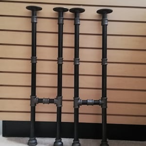 May include: Four black metal pipe legs for a table or shelf. The legs are made of industrial pipe and have a black finish.