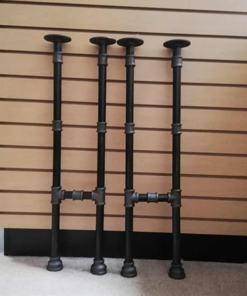 May include: Four black metal pipe legs for a table or shelf. The legs are made of industrial pipe and have a black finish.