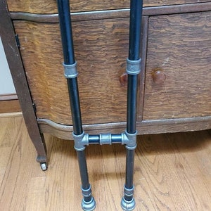 May include: A black metal stand with two vertical pipes and a horizontal connecting pipe. The stand has silver accents on the pipes.